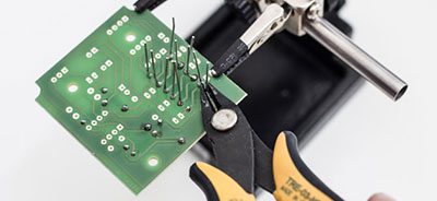 Cutting component leads on a circuit board during assembly of a blood electrification device prototype.